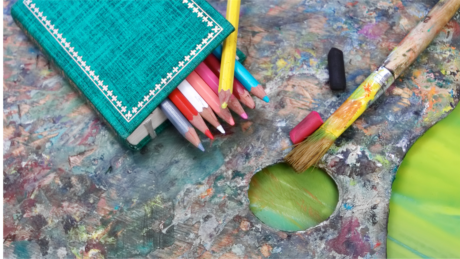 colored pencils and paint brushes on an artist's table